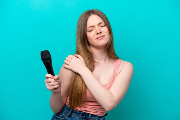 Singer caucasian woman picking up a microphone isolated on blue background suffering from pain in shoulder for having made an effort