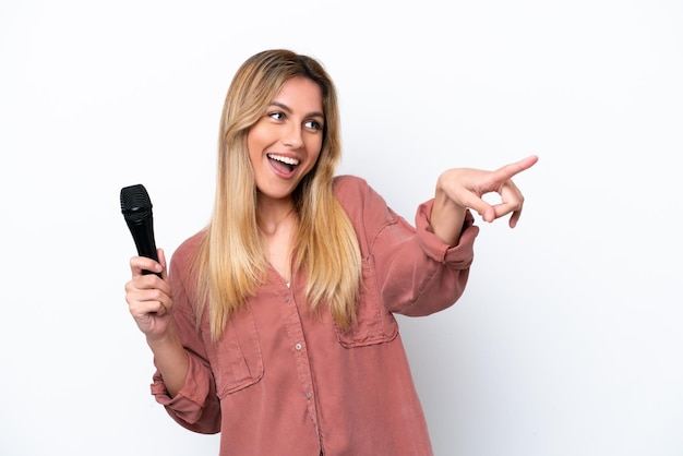 Singer Uruguayan woman picking up a microphone isolated on white background pointing finger to the side and presenting a product