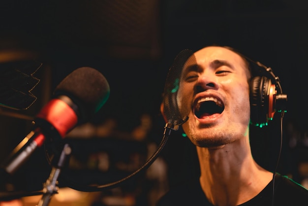 Singer wearing earphones working to record and performance a music voice with professional microphone in audio studio vocalist sing a song with musician artist and sound engineer having live stream