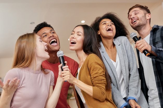 Singing for everyone cheerful multicultured friends singing with microphone while playing karaoke