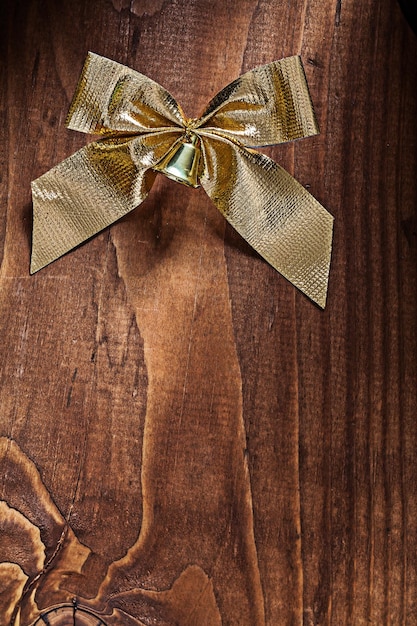 Photo single golden christmas bow with small bell on old wooden board