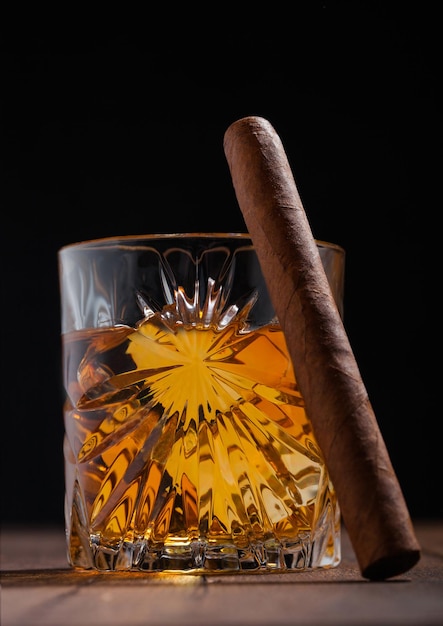 Single malt scotch whiskey in crystal glasses with ice cubes and cuban cigar on wooden table background Macro