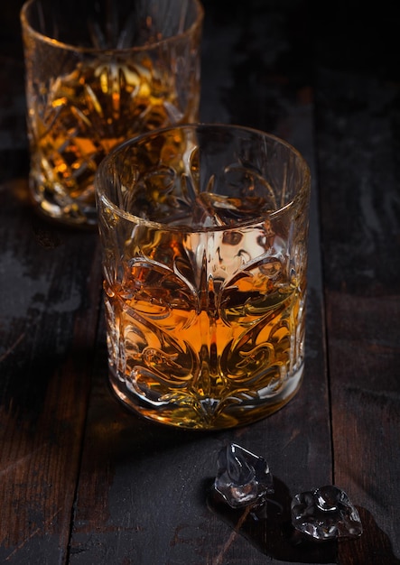 Single malt scotch whiskey in crystal glasses with ice cubes on wooden table background Top view