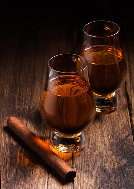 Single malt scotch whiskey in glencairn glasses with cuban cigar on wooden table background Top view