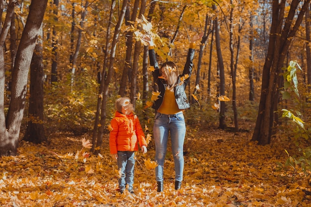 Single parent family playing with autumn leaves in park. Happy mom and son throw autumn leaves up in fall park.