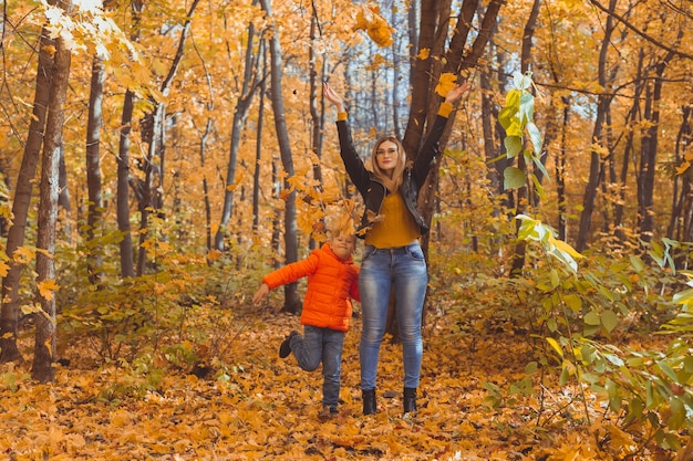 Single parent family playing with autumn leaves in park happy mom and son throw autumn leaves up in