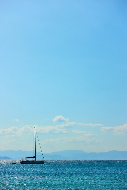 Single sail yacht in the sea near islands and blue sky with clouds. Vertical seascape with large space for your own text