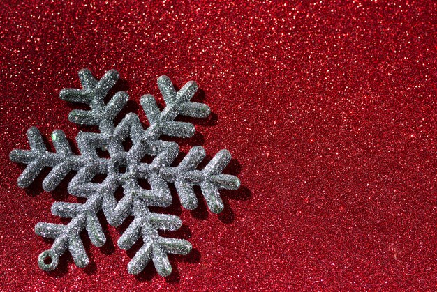 A single shiny snowflake on red glittering background