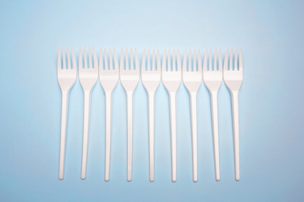 Single-use plastic products: plastic cutlery, cups on bright blue background