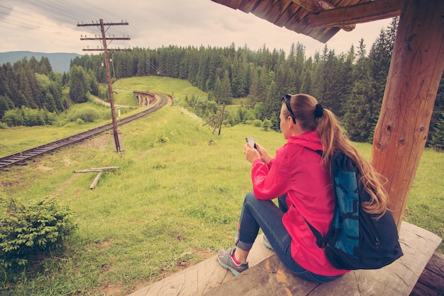 Single woman siting near railway and looking to smartphone