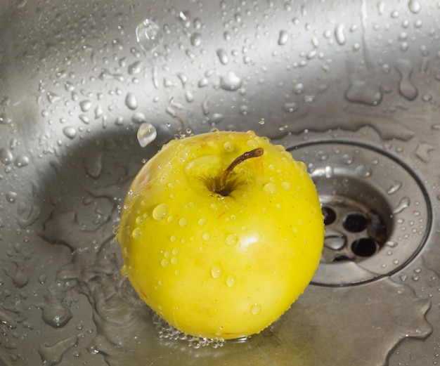 In the sink at the water drops yellow Apple.