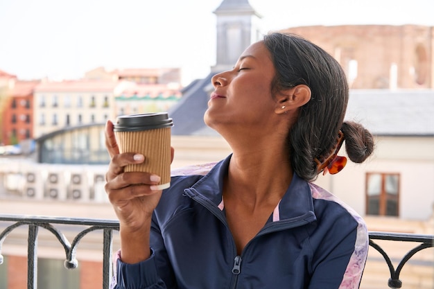 Sipping hot coffee young Indian woman sits on windowsill