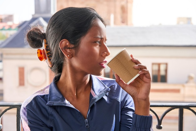 Sipping hot coffee young Indian woman sits on windowsill