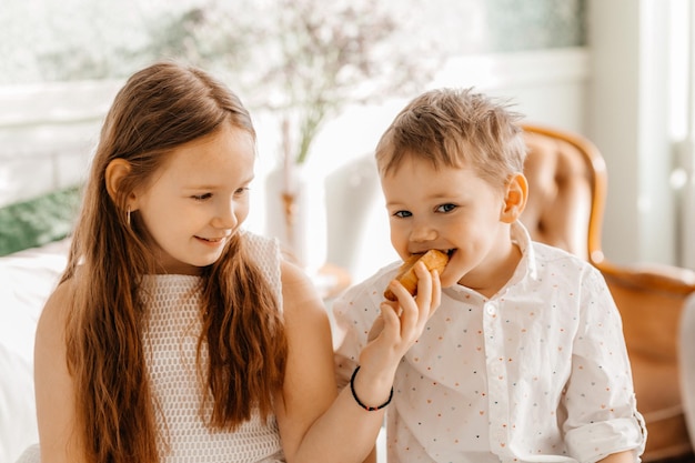 A sister feeds her brother sitting on the bed