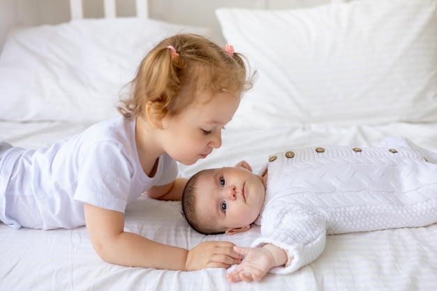 sister gently hugs and kisses a newborn baby in a crib on a white insulated cotton bed two children in the family brother and sister