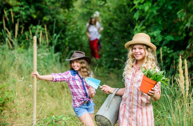 Sisters helping at farm. Eco farming concept. Adorable girls in hats going planting plants. Kids siblings having fun at farm. On way to family farm. Taking care of plants. Girls with gardening tools.