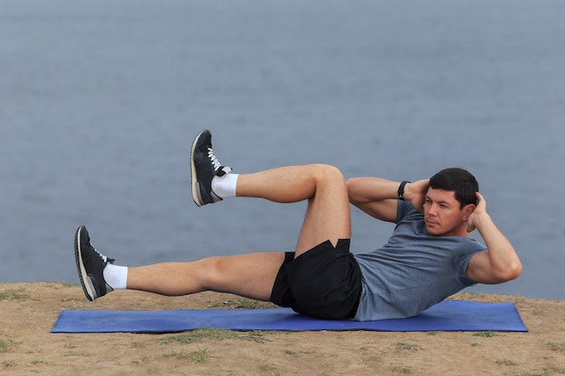 Sit ups - fitness man exercising sit up outside in grass in summer. Fit male athlete working out cross training in summer. Caucasian muscular sports model in his 20s.