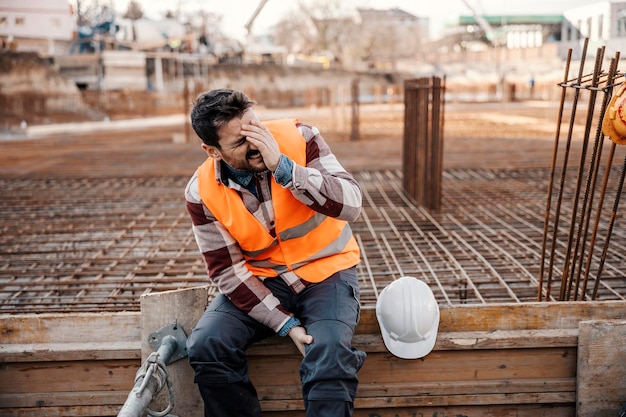 Photo a site worker is sitting on concrete foundation and touching his painful leg