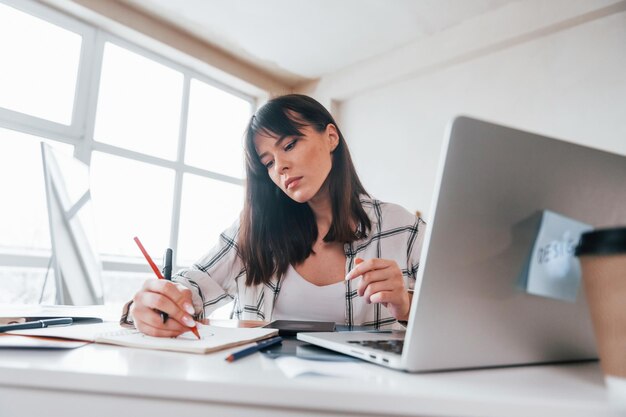 Sits by table Young female freelance worker is indoors in home at daytime