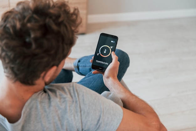 Sits and holds phone in hands Rear view of adult man that is indoors controlling smart home technology