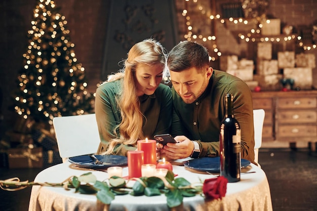 Sits and using phone Young lovely couple have romantic dinner indoors together