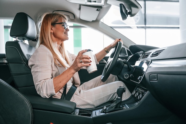 Sitting in the automobile Woman in white formal clothes is in the car dealership