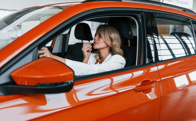 Sitting in the car Woman in formal clothes is indoors in the autosalon