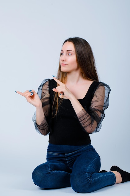 Sitting on floor girl is pointing left with forefingers on white background