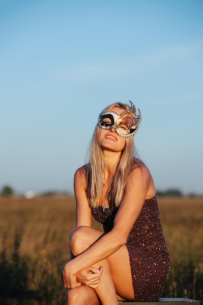 Sitting in front of a dry grass field blond woman in a mask