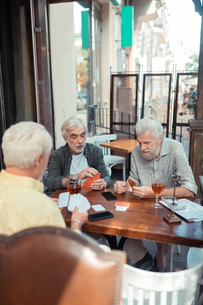 Sitting outside pub. Three aged retired men playing cars while sitting outside pub