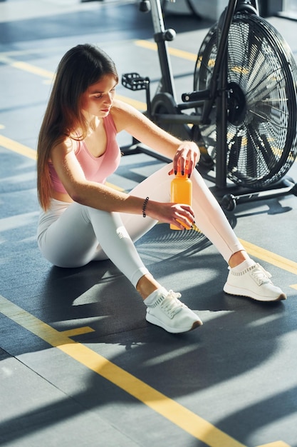 Sitting with bottle of water Beautiful young woman with slim body type is in the gym