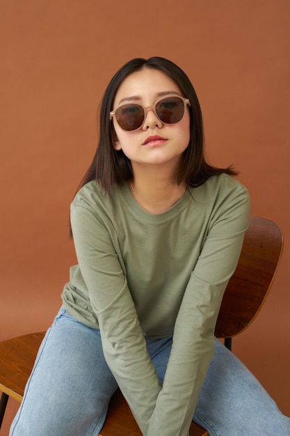 Sitting woman wearing sunglasses on brown background