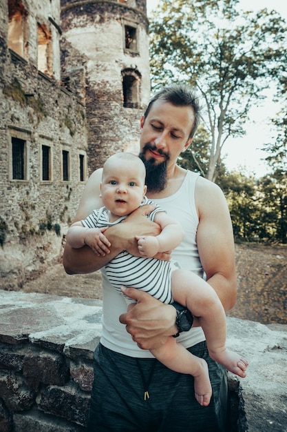 A six-month-old baby in the arms of a father against the backdrop of an old castle