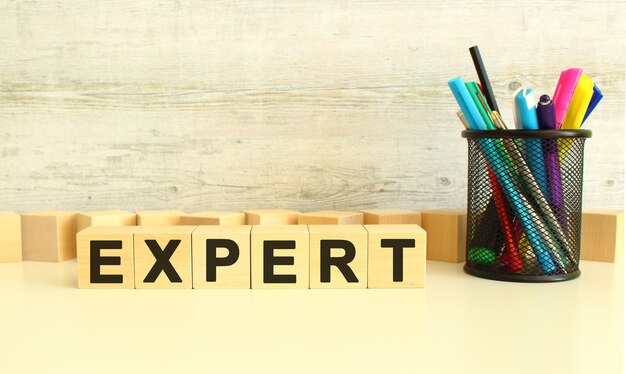 Six stacked wooden cubes with letters EXPERT on work table with colored pencils