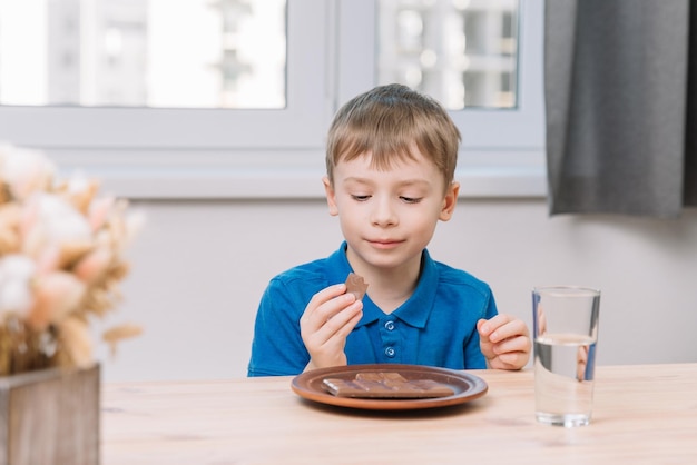 A sixyearold boy looks thoughtfully at a piece of chocolate before eating it