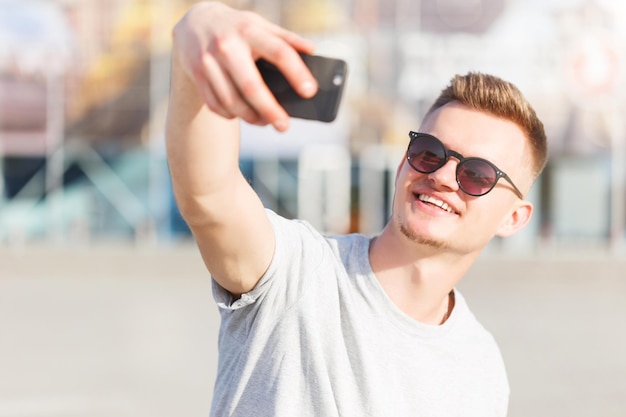 Skateboarder makes selfie before modern building in sunny day