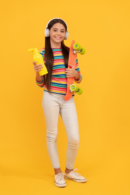 Skateboarding. happy child in headphones with penny board. teen girl listen music. childhood activity. hipster kid skateboarder with plastic water bottle. penny skateboard.