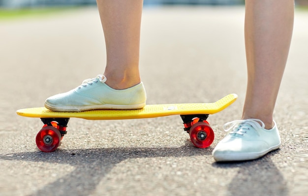 skateboarding, leisure, extreme sport and people concept - close up of teenage girl legs riding short modern cruiser skateboard on road