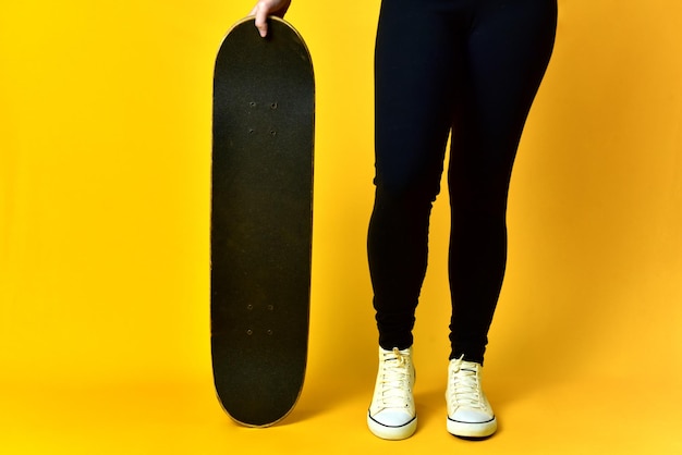 Skater girl legs wearing white sneakers on yellow background