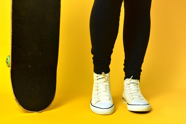 Skater girl legs wearing white sneakers on yellow background