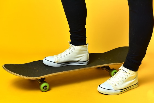 Skater girl legs wearing white sneakers on yellow background