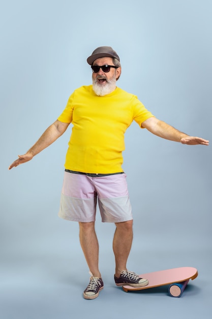 Skater man. Portrait of senior hipster man in eyewear isolated on light blue studio background. Tech and joyful elderly lifestyle concept. Trendy colors, forever youth. Copyspace for your ad.