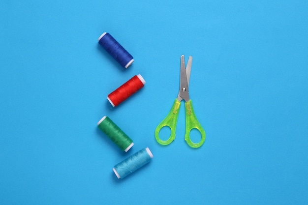 Skeins of colored thread scissors on blue background