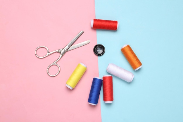 Skeins of colored thread scissors and button on a bluepink pastel background