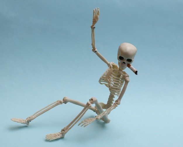 Skeleton smokes a cigarette on blue background. Smoking kills