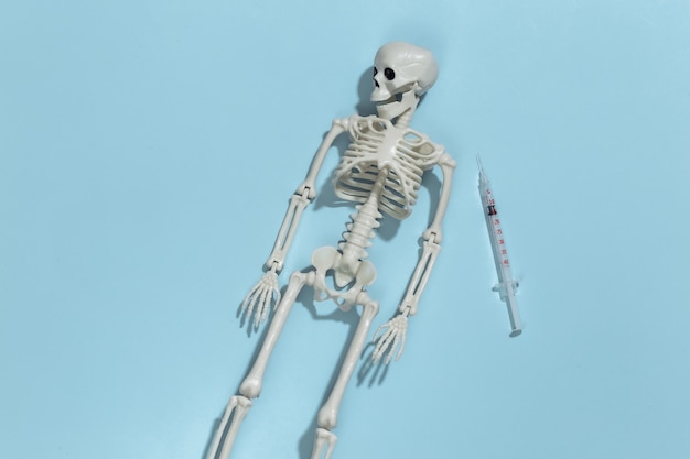 Skeleton and syringe on a blue bright background. Drug addiction. 