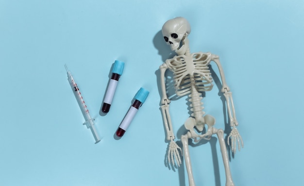 Skeleton, syringe and test tubes with blood on a blue background. 