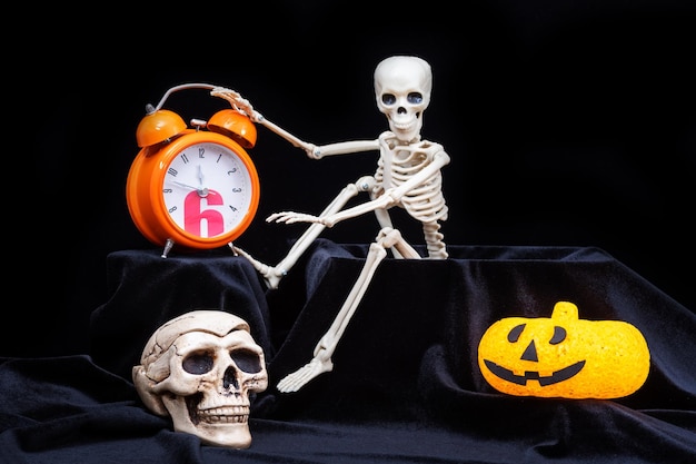 A skeleton waking up crawling out of the grave and turning off an orange alarm clock a pumpkin a skull