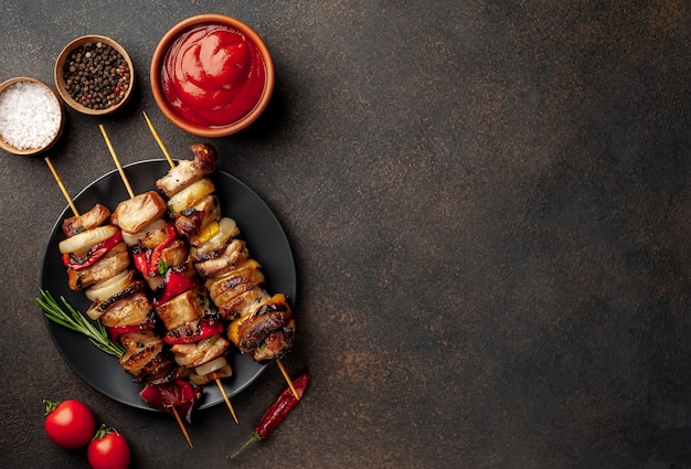 Skewers of meat with grilled vegetables on a plate on a stone background