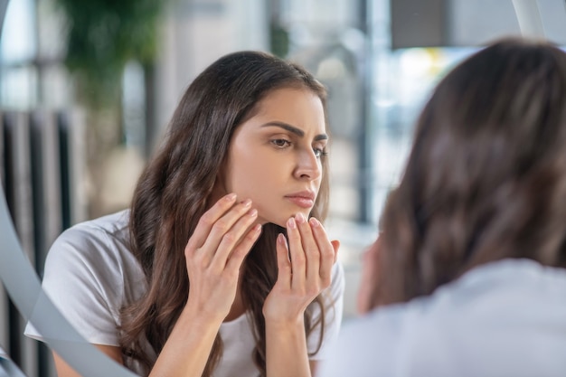 Skicare. A woman attentively checking her skin near the mirror